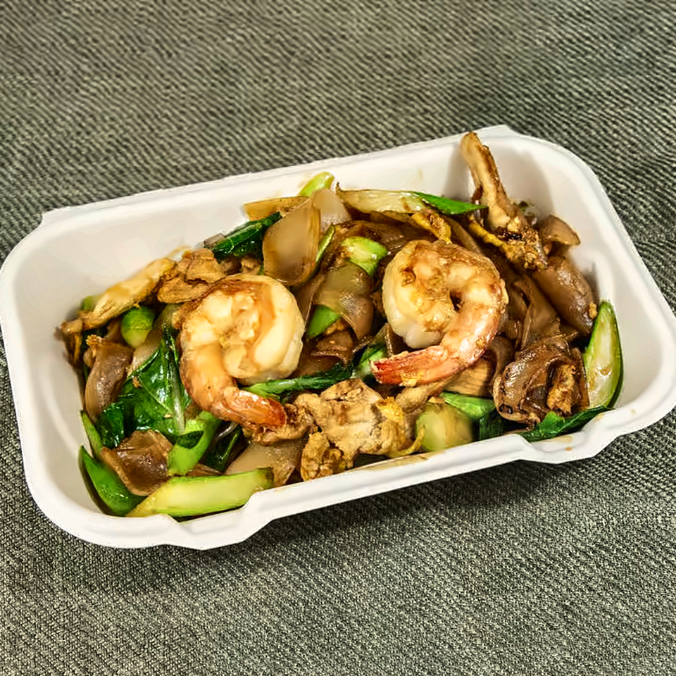 Takeout container filled with shrimp, sliced vegetables, mushrooms, and leafy greens.