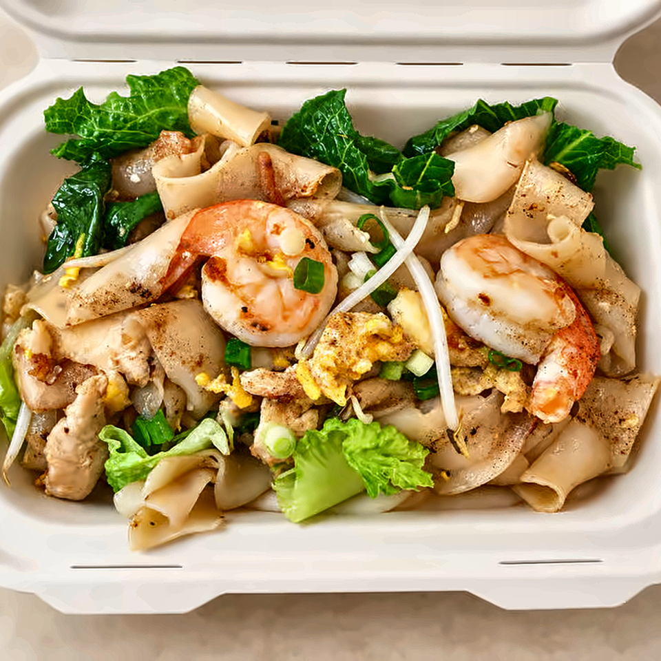 Takeout container filled with stir-fried wide rice noodles, shrimp, chicken, egg, bean sprouts, green onions, and leafy greens.